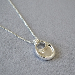 Macro view of silver saddle bag pendant necklace with polished concave metal texture