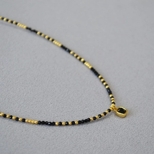 Vue macro d'un collier de perles noires avec un pendentif noir carré bordé d'or chic