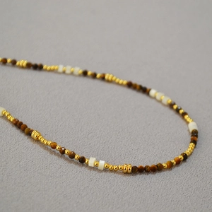 Dettaglio della collana con pietre occhio di tigre, madreperla e perline di metallo oro