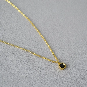Détail macro d'un pendentif carré en spinelle noire avec sertissage doré minimaliste