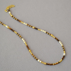 Dettaglio della collana con pietre occhio di tigre marroni e perle dorate su grigio