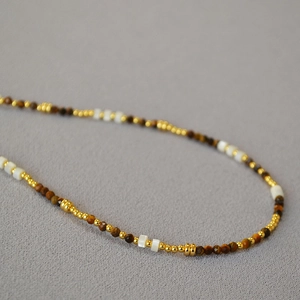Dettaglio di perle occhio di tigre e madreperla con accenti dorati su collana minimalista