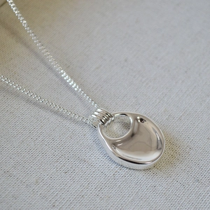 Macro shot of polished silver hollow teardrop pendant and fine cross chain necklace