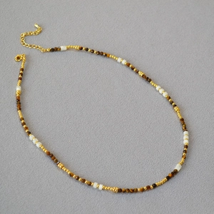 Dettaglio di pietre occhio di tigre e perle di conchiglia con elementi dorati sulla collana