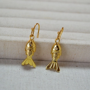 Gold fish drop earrings with articulated tails and sparkling gemstone eyes on a stand