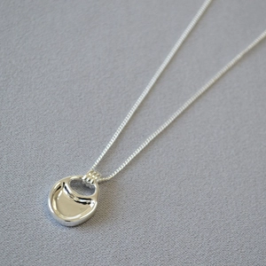 Close-up of polished silver saddle pendant necklace on a textured grey fabric background