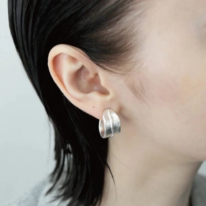 Gros plan de boucles d'oreilles argent mat en forme de C avec texture plissée sur modèle