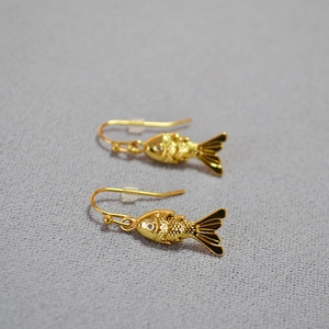 Detailed view of gold fish earrings with intricate scales and sparkling crystal eye