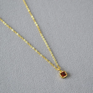 Elegant gold layered necklace with square red zircon pendant on grey fabric