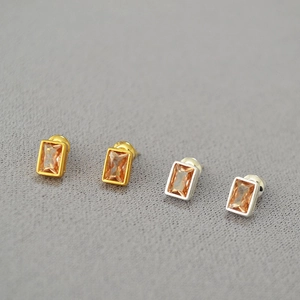 Detailed macro view of gold and silver rectangle stud earrings with amber cubic zirconia