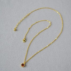 Detailed shot of golden layered necklace with square red zircon pendant and lobster clasp
