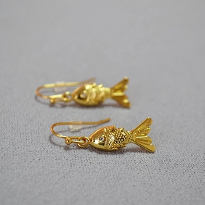 Detailed close-up of gold-plated fish earrings featuring scale textures and white crystals