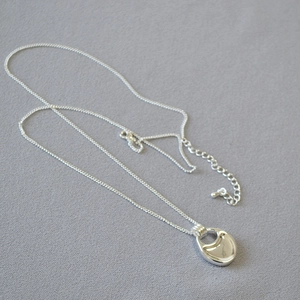 Detail of silver saddle pendant necklace with polished finish on gray textured fabric