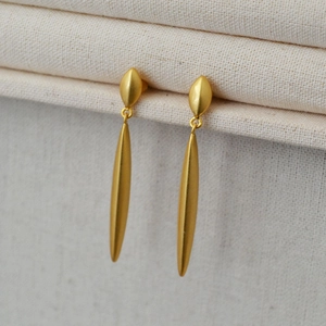 Close-up of elegant gold long drop earrings with a tapered design on textured fabric