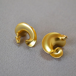 Macro detail of twisted C-shaped gold earrings with a matte brushed metallic finish