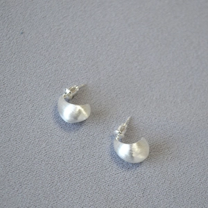 Detailed close-up of C-shaped matte silver earrings with a brushed metallic texture