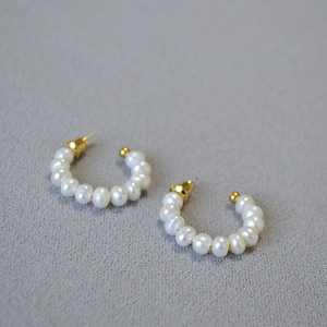 Détail de boucles d'oreilles en perles en forme de C avec tiges dorées sur tissu gris