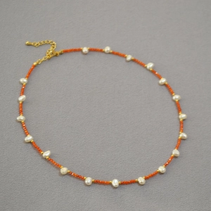 Detail of freshwater pearl necklace with orange beads and golden lobster clasp