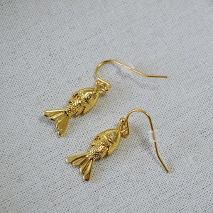 Macro detail of gold-plated fish earrings showing intricate scales and crystal eyes