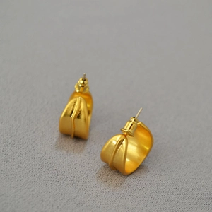 Détail de boucles d'oreilles dorées mates en forme de C avec texture en relief