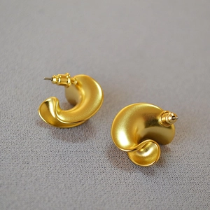 Macro detail of twisted C-shaped gold earrings with textured matte finish and secure backs