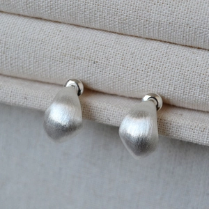 Macro view of teardrop stud earrings featuring a brushed metallic silver finish texture