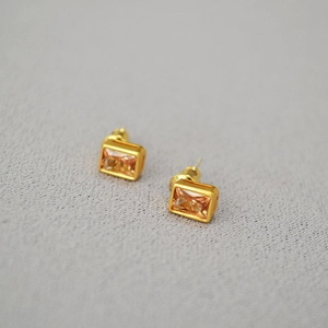Elegant gold earrings with champagne rectangular crystals on dark velvet background