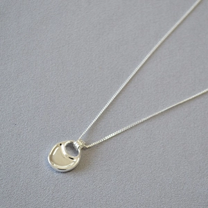 Macro shot of polished silver saddle bag pendant with a minimalist hollow oval design