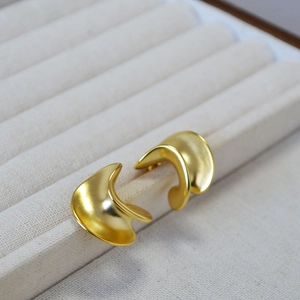 Detail of chunky gold irregular C-shape earrings with a matte brushed metallic finish
