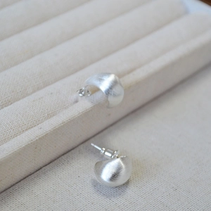 Brushed silver water drop studs on jewelry display with matte metallic texture