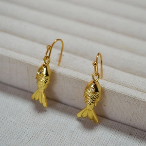 Macro shot of gold-plated fish earrings with detailed scales on a grey fabric display