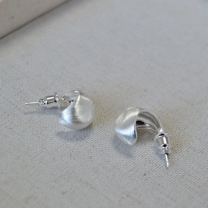 Macro shot of silver drop earrings with matte brushed finish on textured cloth