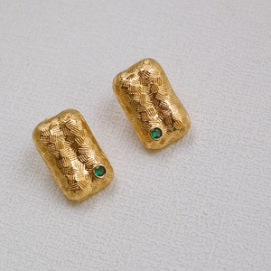 Detail of gold-plated brass stud earrings with woven texture and emerald green gemstones