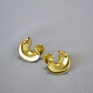 Macro detail of gold-plated twisted C-shape earrings with a matte brushed metal finish