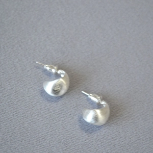 Detail of matte silver teardrop earrings with brushed metal texture and minimalist arc design
