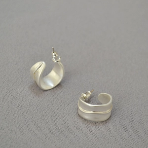 Détail des boucles d'oreilles irrégulières en forme de C argent mat sur tissu