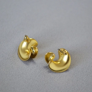 Detailed macro shot of matte gold irregular C-shape earrings on light grey fabric texture