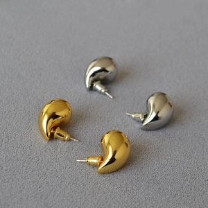 Macro detail of polished gold and silver hollow teardrop earrings on textured fabric