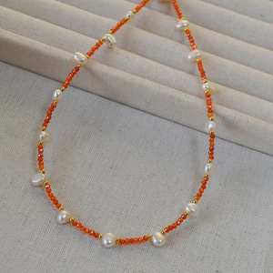 Detailed macro view of beaded necklace with orange faceted beads and baroque pearls