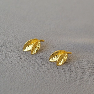Detailed macro view of gold leaf earrings with textured hammered finish on grey fabric
