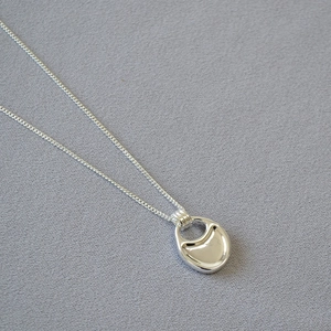 Macro detail of polished silver bean pendant on a fine chain with a glossy mirror finish