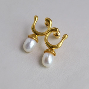 Macro view of gold-plated brass drop earrings with white pearls and fluid design