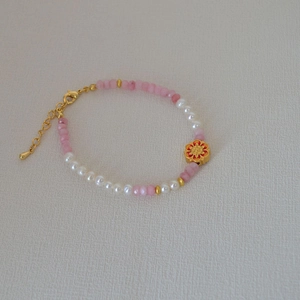 Détail d'un bracelet perlé avec pierres roses, perles blanches et fleur en émail doré