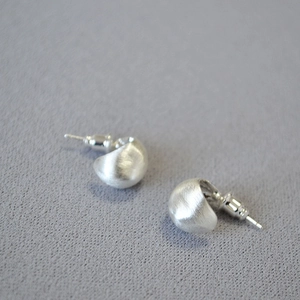 Minimalist silver teardrop earrings with a matte brushed finish on light grey fabric