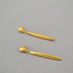 Detail of matte gold minimalist long cone earrings with brushed metal finish