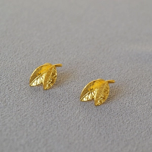 Macro view of gold leaf stud earrings with detailed vein texture on dark grey fabric