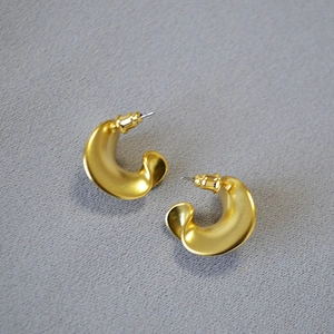 Detail of twisted C-shaped earrings with a matte brushed gold finish and sculpted design