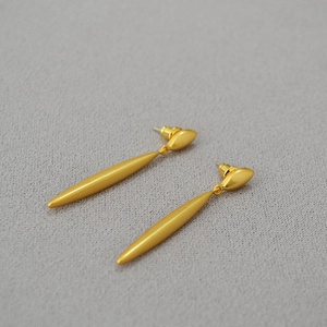 Detail of long matte gold streamline earrings with elegant textured surface finish
