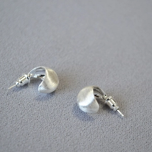 Macro shot of silver C-shaped stud earrings with brushed matte and polished finish