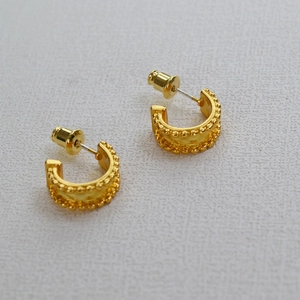 Detailed view of gold plated C-shaped earrings with beaded texture and sphere backing
